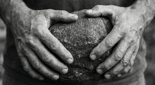 Weathered hands firmly clasping a heavy, rough stone. Visualizing the 'Heavy Bone' archetype, the weight of responsibility, and the strength of resilience - MINDNESS.